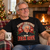 Father Jack-inspired Christmas T-shirt worn by an adult man beside a festive fireplace